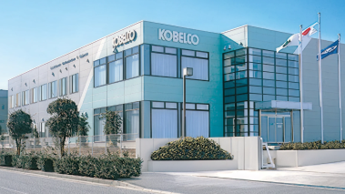 コベルコ建機のロゴが掲げられた青緑色のオフィスビル外観。